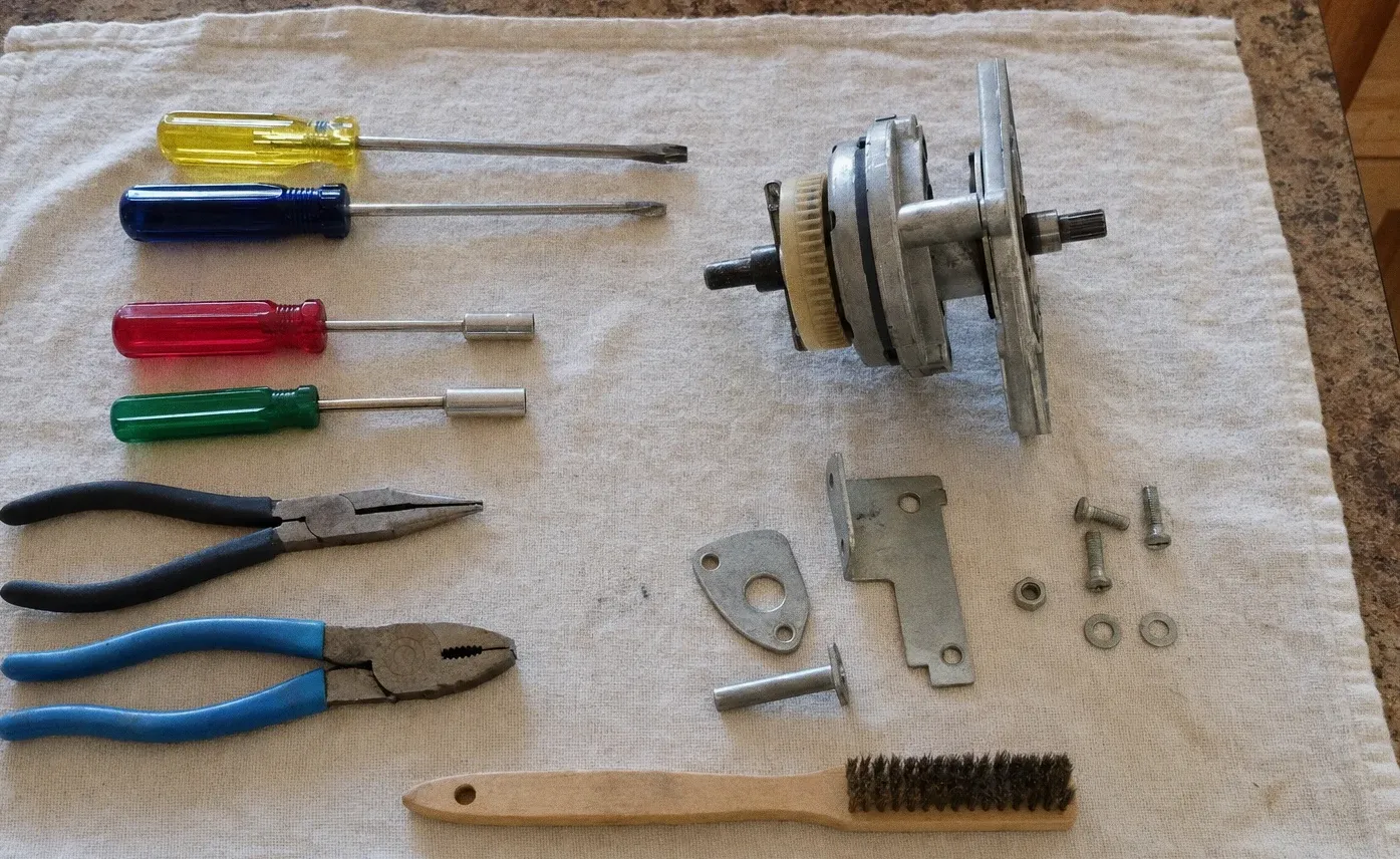 Screwdrivers, pliers and a wire brush on a towel beside a blower motor assembly with its fan wheel and mounting brackets